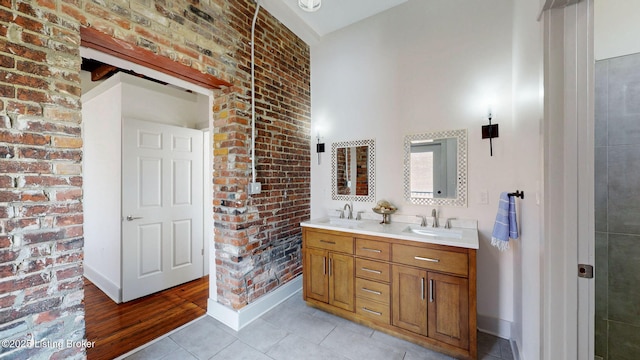 full bathroom with double vanity, tile patterned flooring, brick wall, and a sink