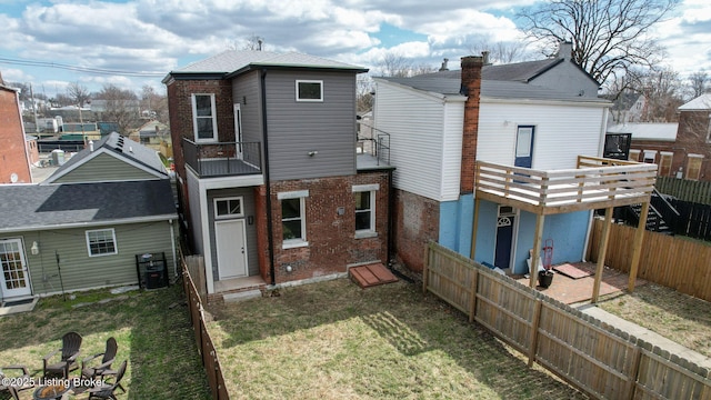 rear view of house with a yard, brick siding, a fenced backyard, and a balcony