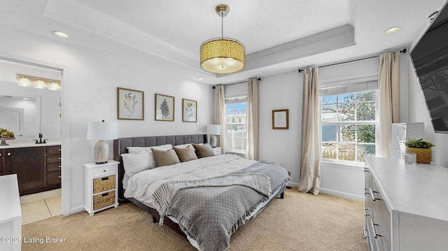 bedroom featuring recessed lighting, light carpet, baseboards, a raised ceiling, and ensuite bath