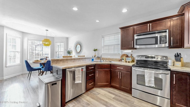 kitchen featuring stainless steel appliances, a peninsula, a sink, light countertops, and light wood-type flooring