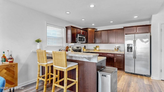 kitchen with stainless steel appliances, light countertops, light wood-style flooring, and a kitchen breakfast bar