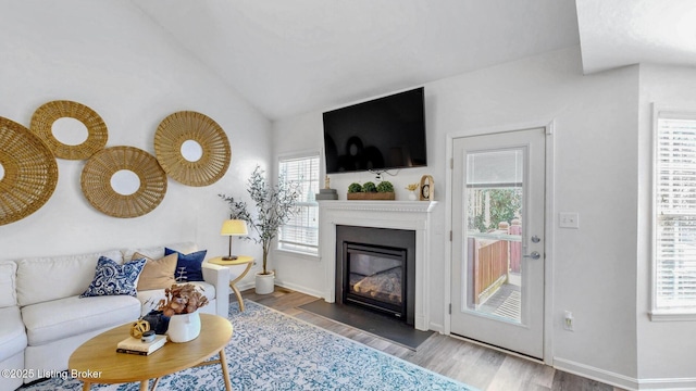 living area with lofted ceiling, a fireplace with flush hearth, wood finished floors, and baseboards