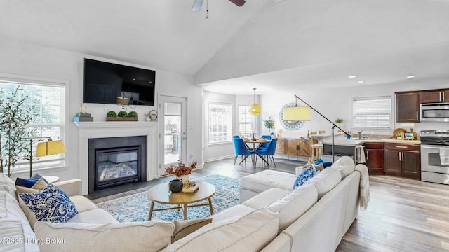 living area with ceiling fan, high vaulted ceiling, light wood-style flooring, recessed lighting, and a glass covered fireplace