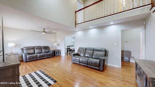 living area featuring light wood finished floors, a ceiling fan, a high ceiling, and baseboards