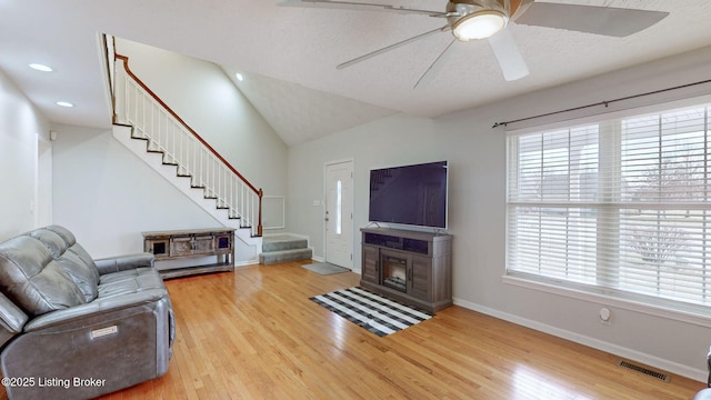 living room featuring visible vents, ceiling fan, stairway, a fireplace with flush hearth, and wood finished floors