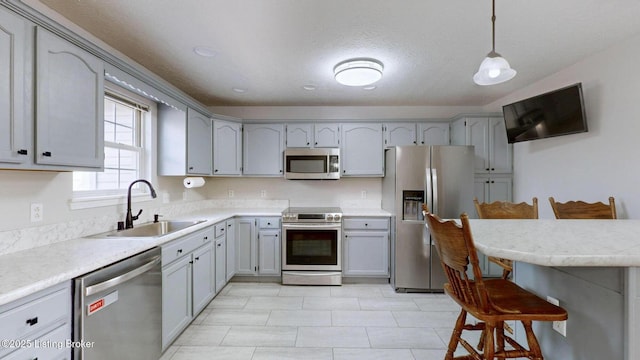 kitchen with a breakfast bar area, a sink, stainless steel appliances, pendant lighting, and a textured ceiling