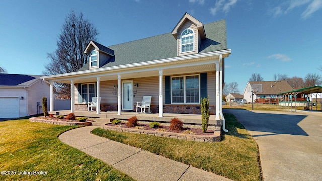 new england style home featuring a porch, a front yard, roof with shingles, stone siding, and driveway