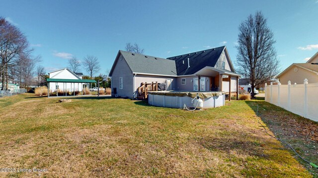 rear view of house with a covered pool, a lawn, and fence