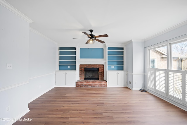 unfurnished living room featuring wood finished floors, a ceiling fan, baseboards, ornamental molding, and a brick fireplace