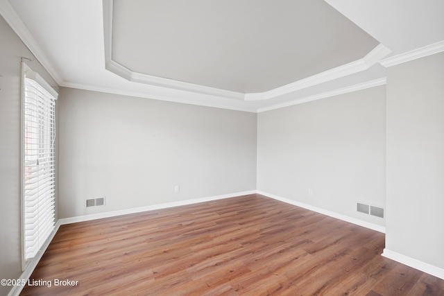 empty room featuring wood finished floors, visible vents, and crown molding