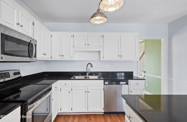 kitchen featuring wood finished floors, a sink, white cabinetry, appliances with stainless steel finishes, and dark countertops