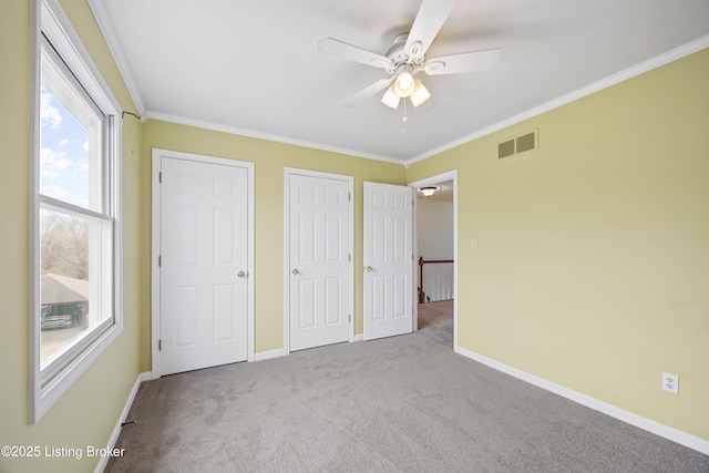 unfurnished bedroom featuring visible vents, crown molding, baseboards, and two closets