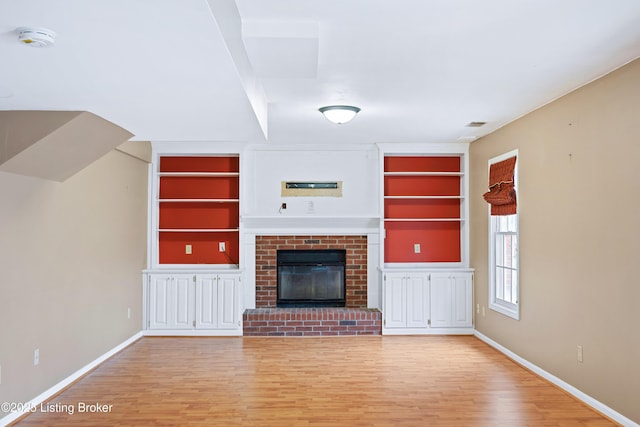 unfurnished living room featuring light wood-style floors, built in shelves, a fireplace, and baseboards