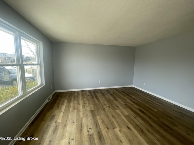 spare room with dark wood finished floors, plenty of natural light, and baseboards