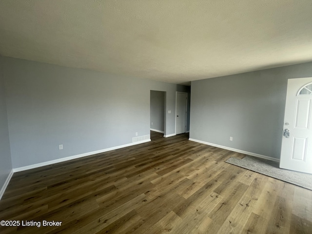 spare room with dark wood-style floors, visible vents, a textured ceiling, and baseboards