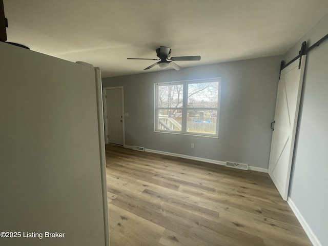 spare room with light wood finished floors, visible vents, a barn door, a ceiling fan, and baseboards