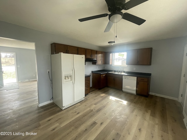 kitchen featuring white appliances, baseboards, dark countertops, light wood-type flooring, and a sink