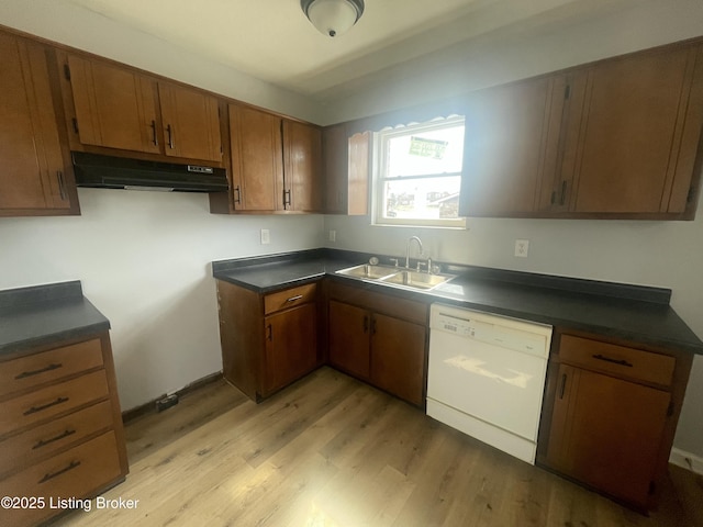 kitchen featuring dark countertops, brown cabinetry, white dishwasher, a sink, and under cabinet range hood