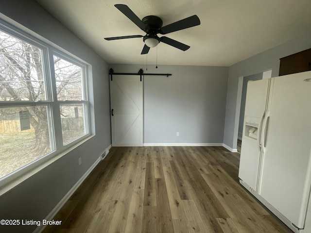 interior space with a barn door, baseboards, ceiling fan, and wood finished floors