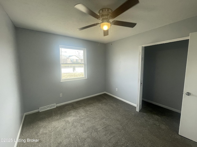 unfurnished bedroom featuring visible vents, dark carpet, a textured ceiling, and baseboards