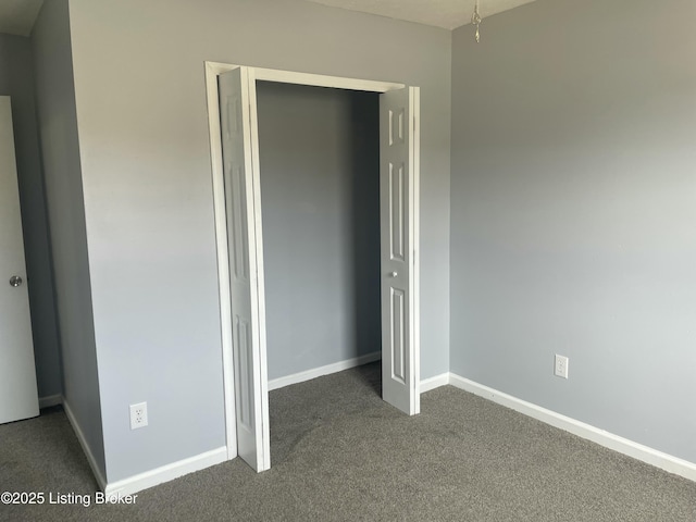 unfurnished bedroom featuring baseboards, dark carpet, and a closet