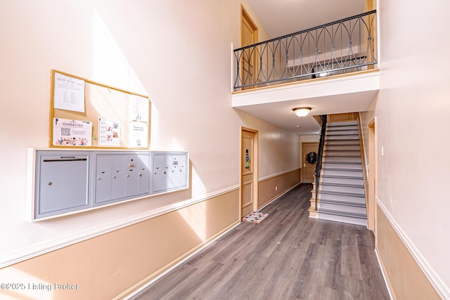 corridor featuring a high ceiling, stairway, wood finished floors, and mail area