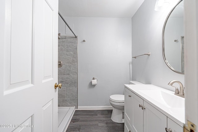 bathroom featuring baseboards, tiled shower, toilet, wood finished floors, and vanity