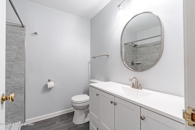 bathroom featuring a shower, toilet, vanity, wood finished floors, and baseboards