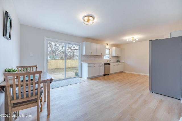 kitchen with light wood-style flooring, stainless steel appliances, white cabinets, light countertops, and backsplash