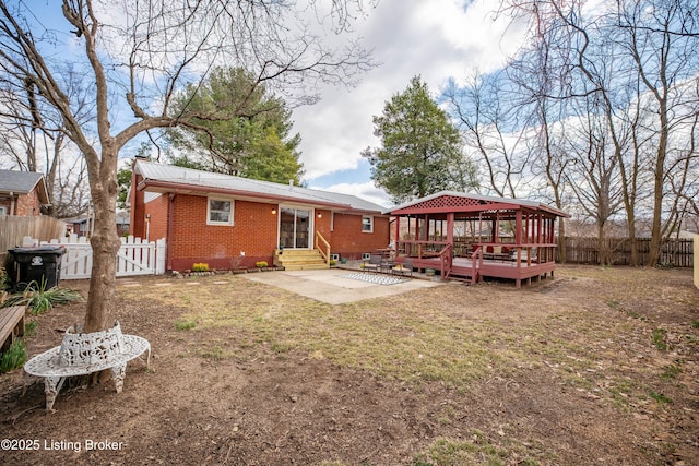 back of property with entry steps, metal roof, a fenced backyard, brick siding, and a gazebo