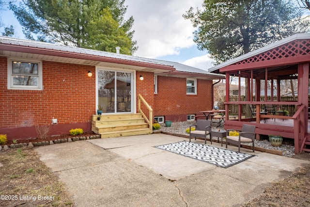 back of house with entry steps, metal roof, brick siding, and a patio