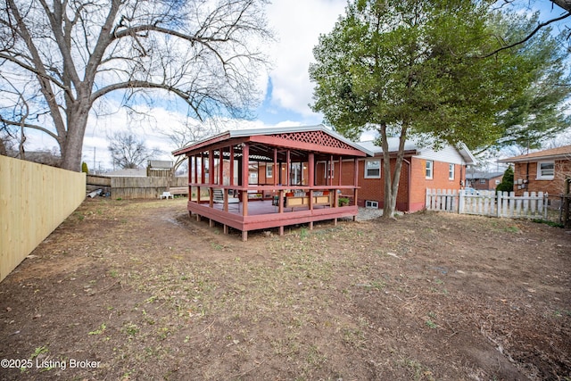 rear view of property featuring brick siding, a fenced backyard, and a wooden deck