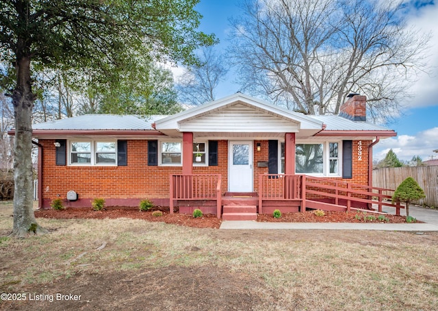 view of front of house with brick siding, a chimney, a front yard, metal roof, and fence