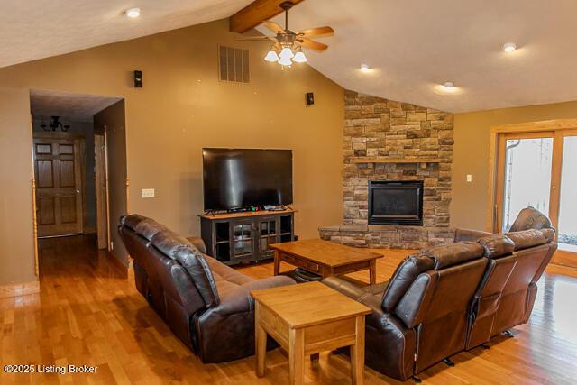 living area featuring a stone fireplace, beamed ceiling, visible vents, and light wood-style floors