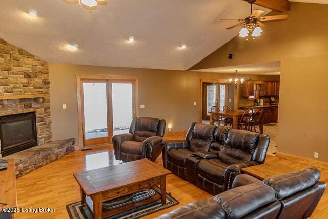 living room with light wood-style flooring, ceiling fan with notable chandelier, and a stone fireplace