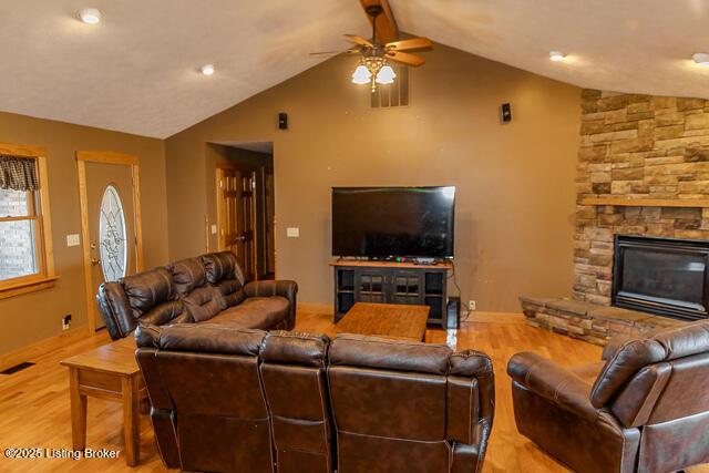 living room featuring ceiling fan, a fireplace, wood finished floors, visible vents, and vaulted ceiling