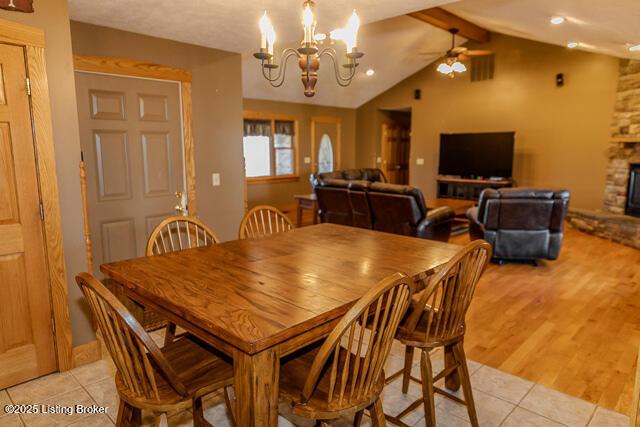 dining area with vaulted ceiling with beams, light wood-style floors, ceiling fan with notable chandelier, and a stone fireplace