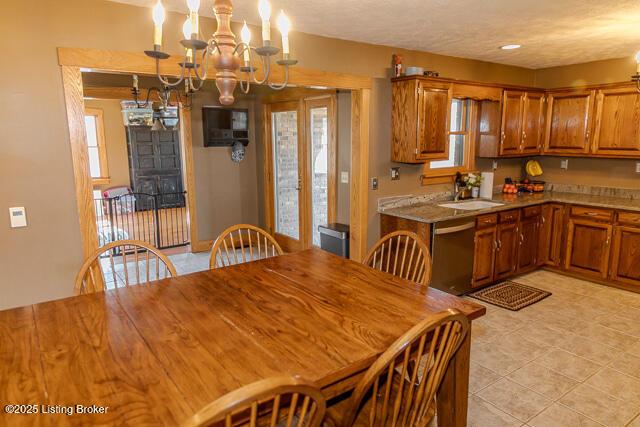 kitchen featuring light tile patterned floors, stainless steel dishwasher, brown cabinets, decorative light fixtures, and an inviting chandelier