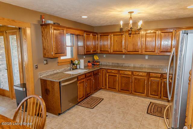 kitchen with brown cabinets, stainless steel appliances, light countertops, an inviting chandelier, and a sink