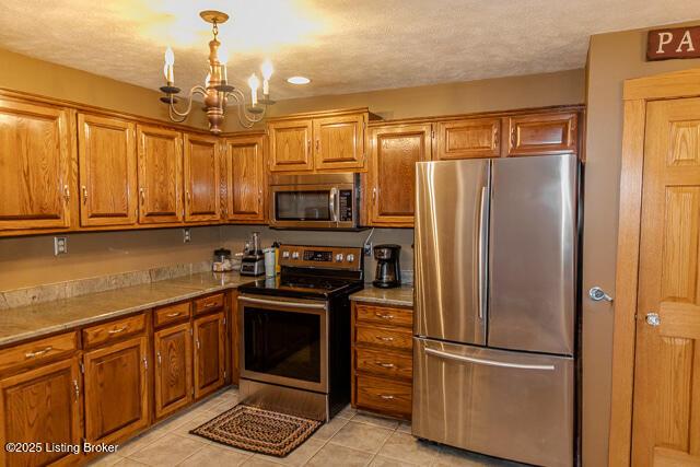 kitchen with brown cabinets, a notable chandelier, decorative light fixtures, light tile patterned floors, and stainless steel appliances