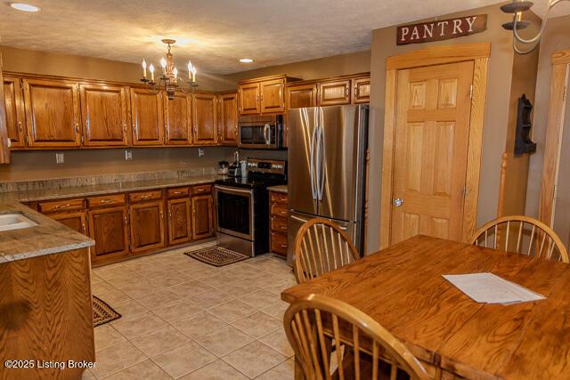 kitchen with appliances with stainless steel finishes, pendant lighting, brown cabinetry, and light tile patterned floors