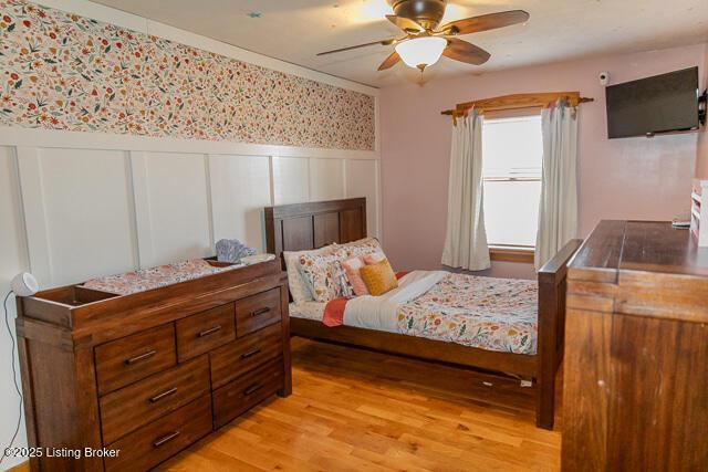 bedroom with a wainscoted wall, ceiling fan, wallpapered walls, and light wood-style floors