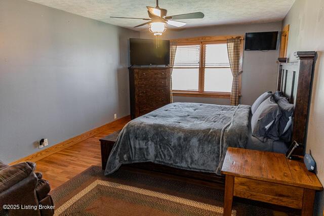 bedroom with a ceiling fan, a textured ceiling, baseboards, and wood finished floors