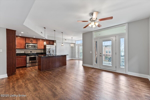 kitchen with dark wood-style flooring, hanging light fixtures, appliances with stainless steel finishes, dark countertops, and open floor plan