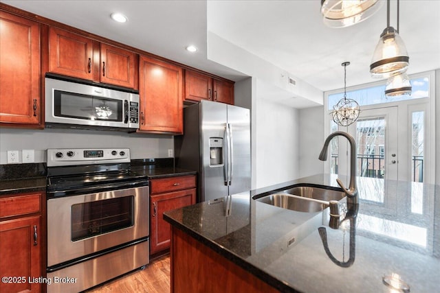 kitchen with pendant lighting, a sink, stainless steel appliances, dark stone counters, and light wood finished floors