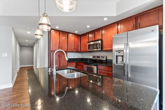 kitchen with a sink, dark wood finished floors, stainless steel appliances, dark stone counters, and baseboards