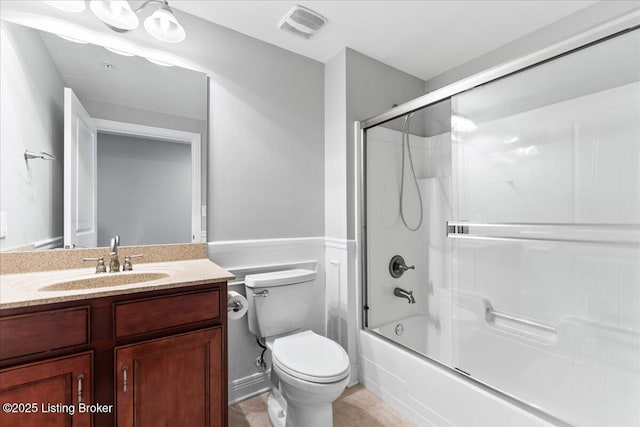 bathroom featuring vanity, visible vents, enclosed tub / shower combo, wainscoting, and toilet