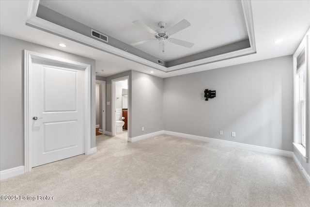 empty room with baseboards, visible vents, a raised ceiling, and light carpet