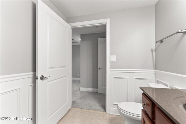 bathroom with a decorative wall, toilet, vanity, and a wainscoted wall