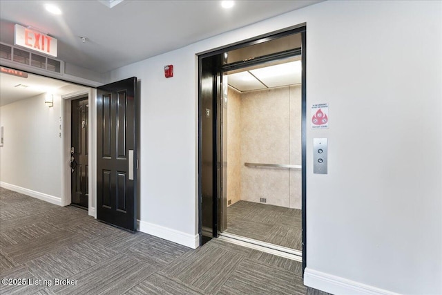 hallway with elevator, carpet flooring, and baseboards